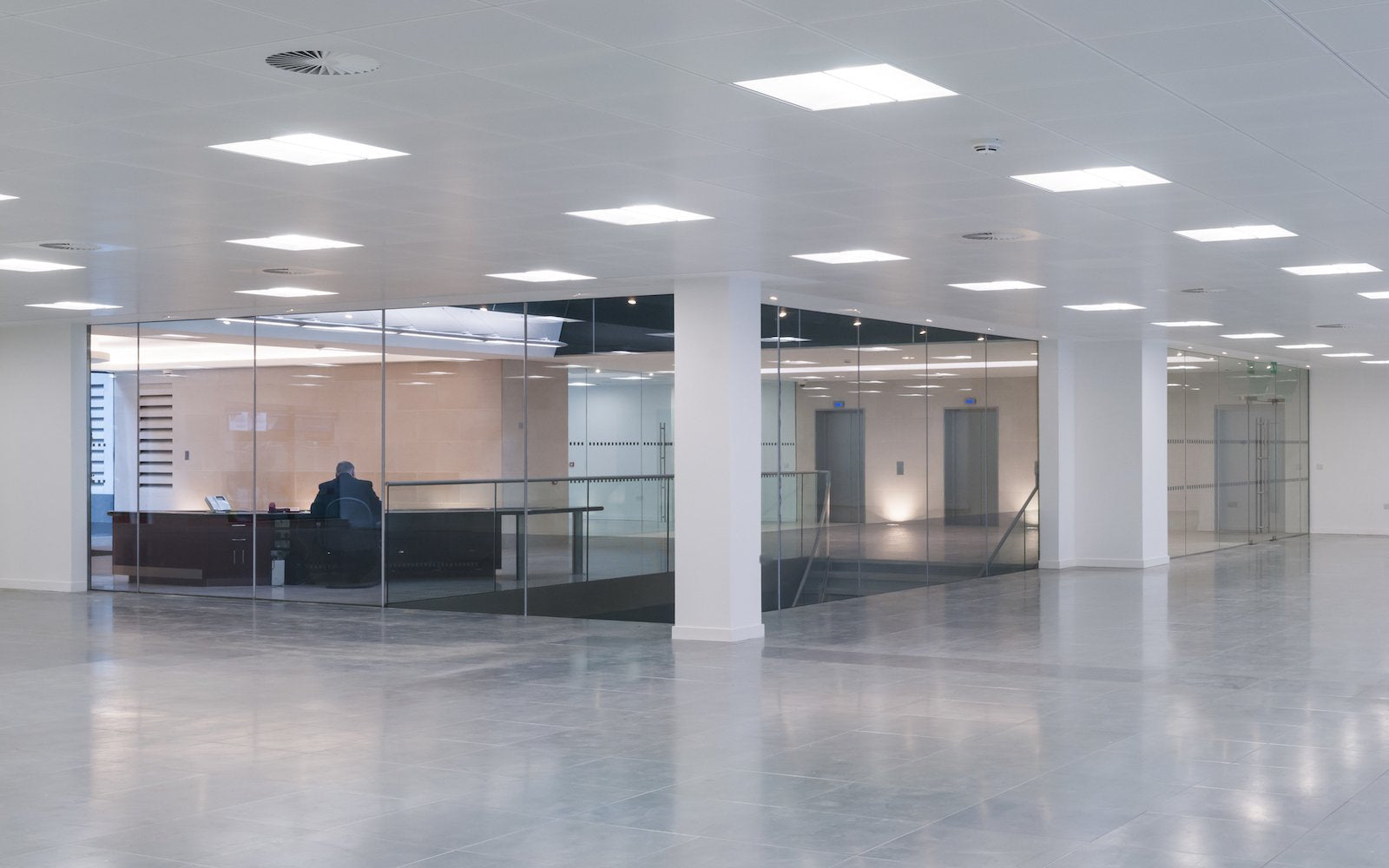 2x2 LED Troffer lights installed in a modern office with dark grey concrete floors, glass walls, and a stairway leading downstairs, providing bright, uniform illumination.