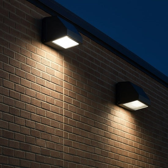 NCLTG LED full cutoff wall pack fixtures mounted on the side of a commercial brick building, providing bright and even outdoor illumination at dusk.