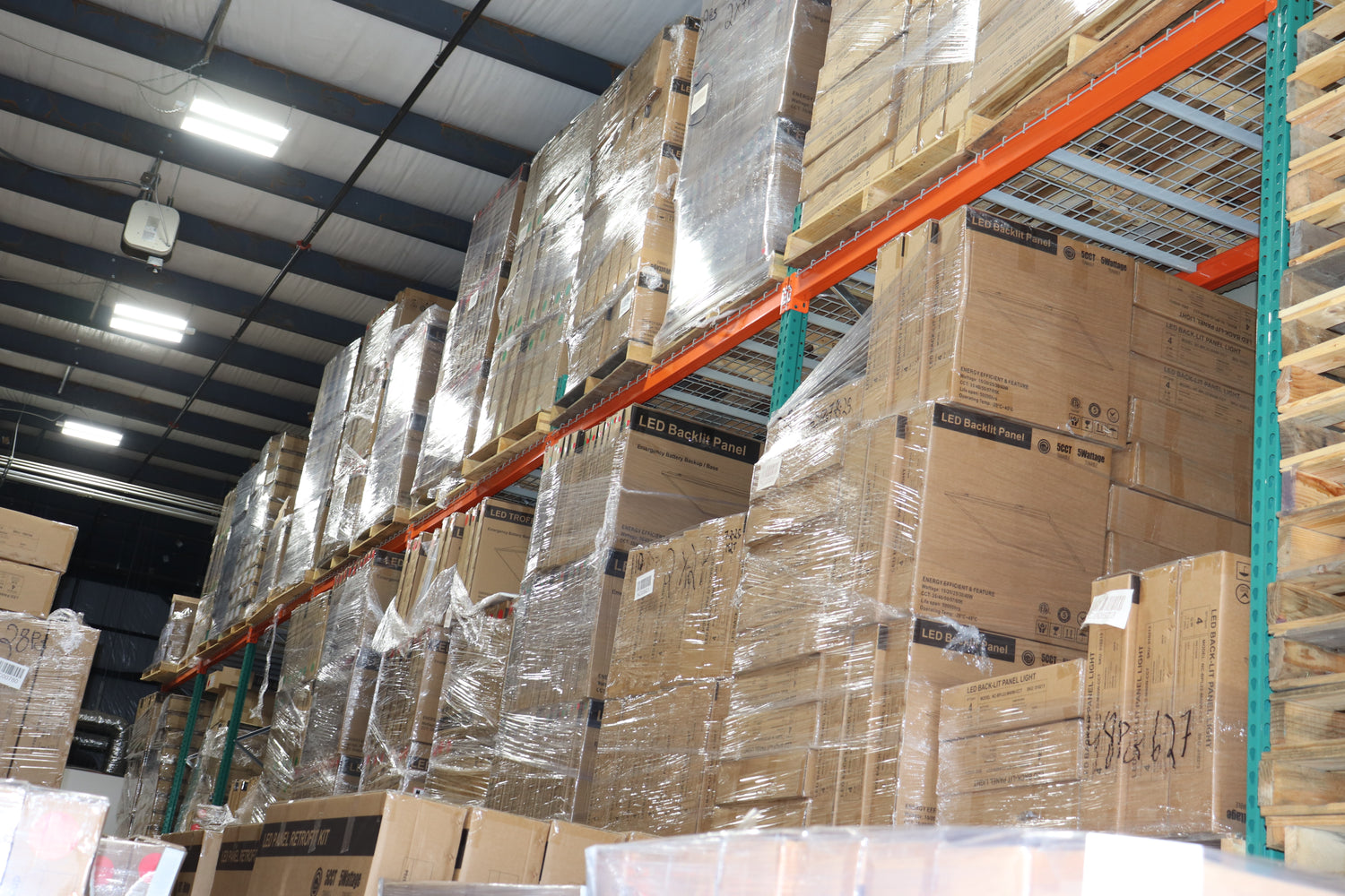 Interior view of the NCLTG Charlotte warehouse with shrink-wrapped LED panel lights and troffer fixtures neatly organized on industrial storage racks.